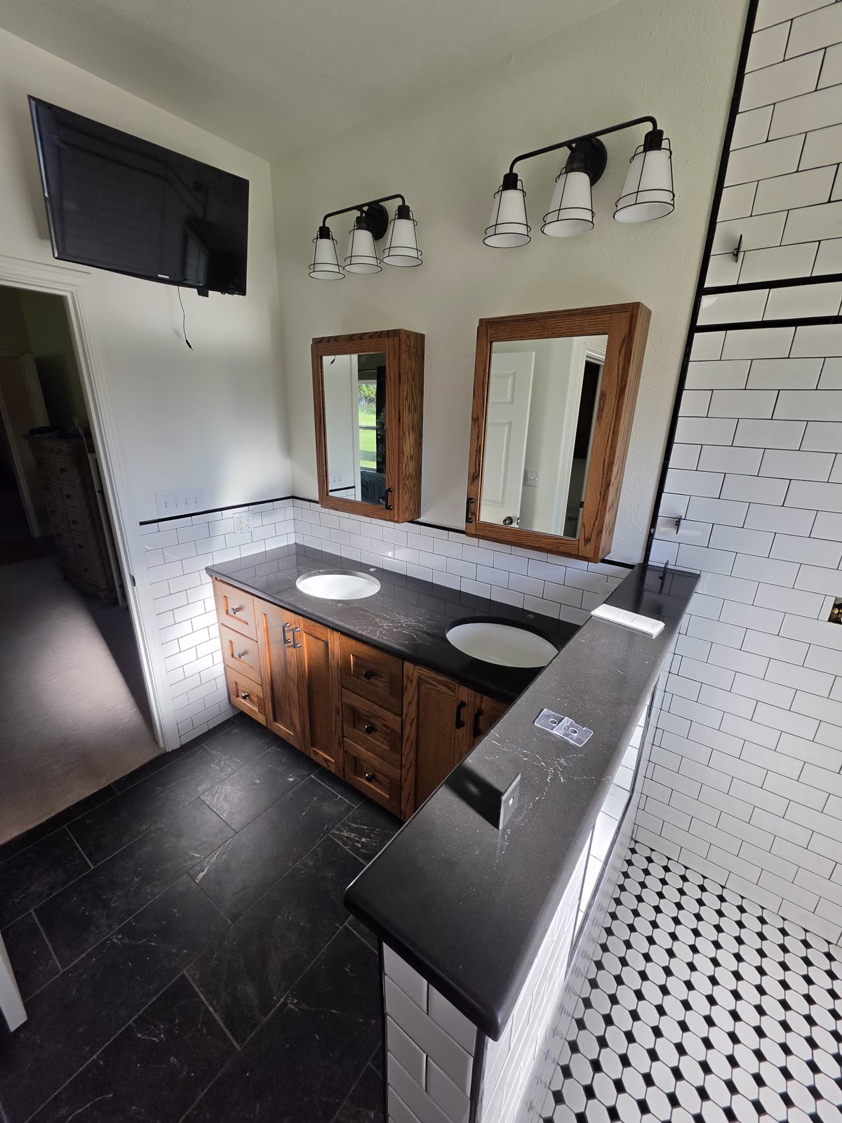 Oak vanity bathroom with a black countertop and black-and-white hex tile flooring