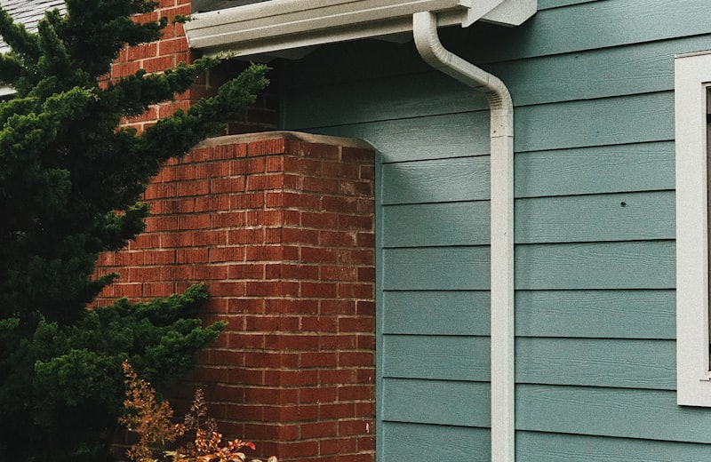 White gutter and downspout on a home with blue siding and a brick chimney