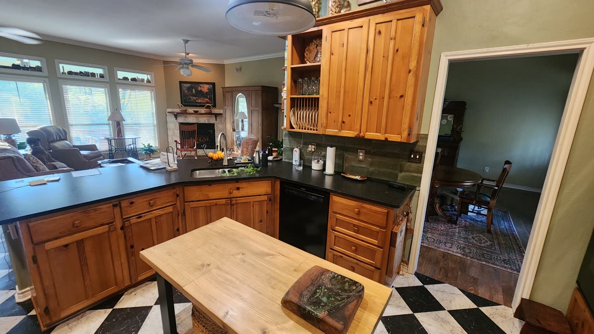 Kitchen with wood-tone cabinetry and black countertops opening into the living room